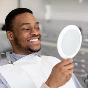 Man smiling while looking at reflection in handheld mirror