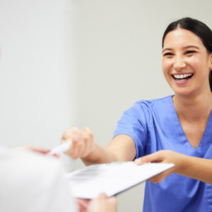 Smiling dental assistant handing patient form
